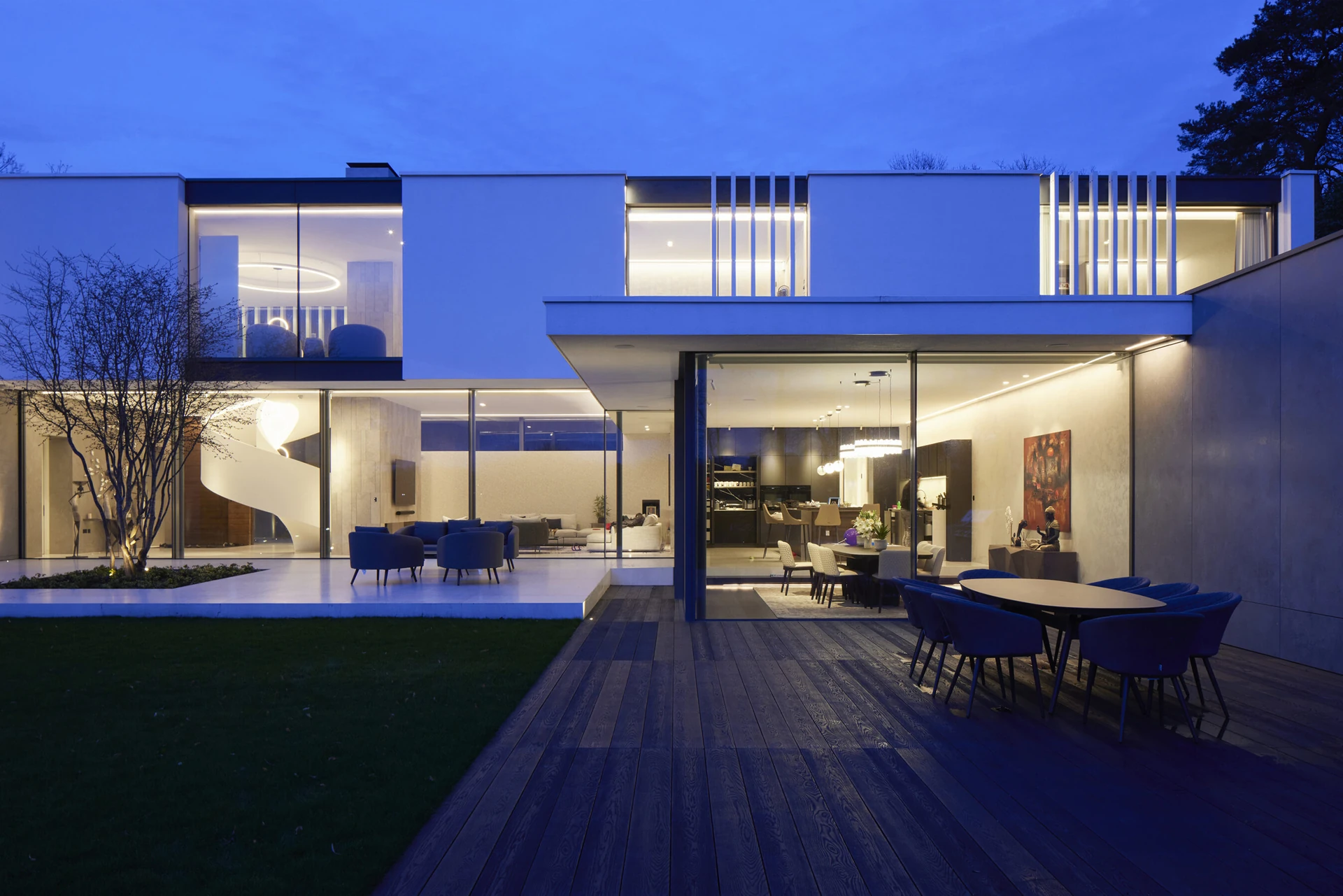 Contemporary home in Radlett at dusk with illuminated floor-to-ceiling glazing and a garden terrace